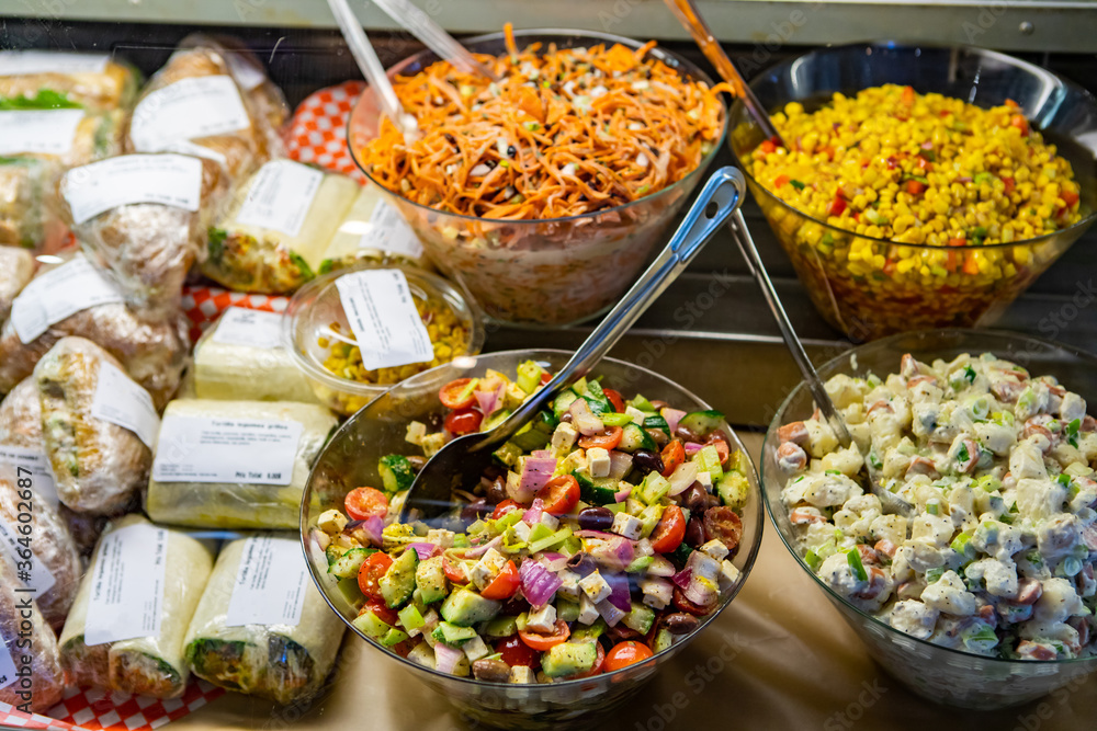 Variety of healthy and delicious fresh salads dishes and sandwiches ready for customers on the display refrigerator of a bistro buffet restaurant.