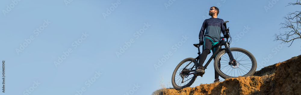 Fototapeta premium Cyclist in shorts and jersey on a modern carbon hardtail bike with an air suspension fork standing on a cliff against the background of fresh green spring forest