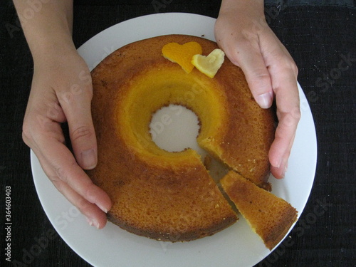 Manos de mujer alrededor de torta de maíz redonda con decoración de dos corazones con un pedacito cortado en cuña y separado. Plato blanco sobre fondo negro photo
