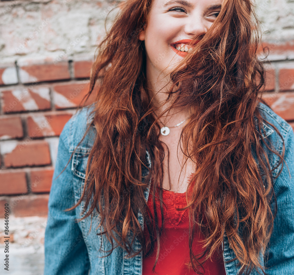 Sincerely smiling Red curled hair caucasian teen girl with applied red lipstick lips with blue eyes fashion vertical portrait on the red brick wall background. Natural people beauty concept image. Sincerely smiling Red curled hair caucasian teen girl with applied red lipstick lips with blue eyes fashion vertical portrait on the red brick wall background. Natural people beauty concept image.