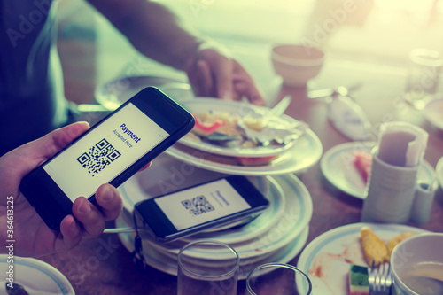 Hand using smart phone to scan QR code on tag with blurry many dishes after eating in restaurant to accepted generate digital pay without money. Qr code payment concept.