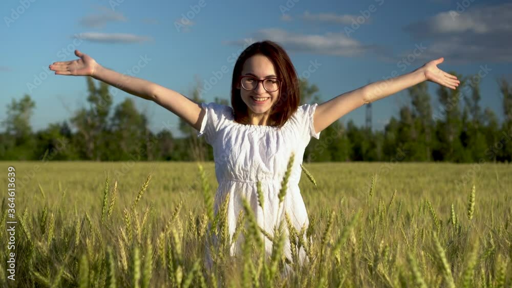 A young woman in a white dress jumps out of a green wheat field. The girl suddenly appears and smiles. A young woman in a white dress jumps out of a green wheat field. The girl suddenly appears and smiles.