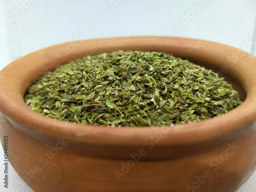 Green oregano in a small bowl. On top of a white wood table 