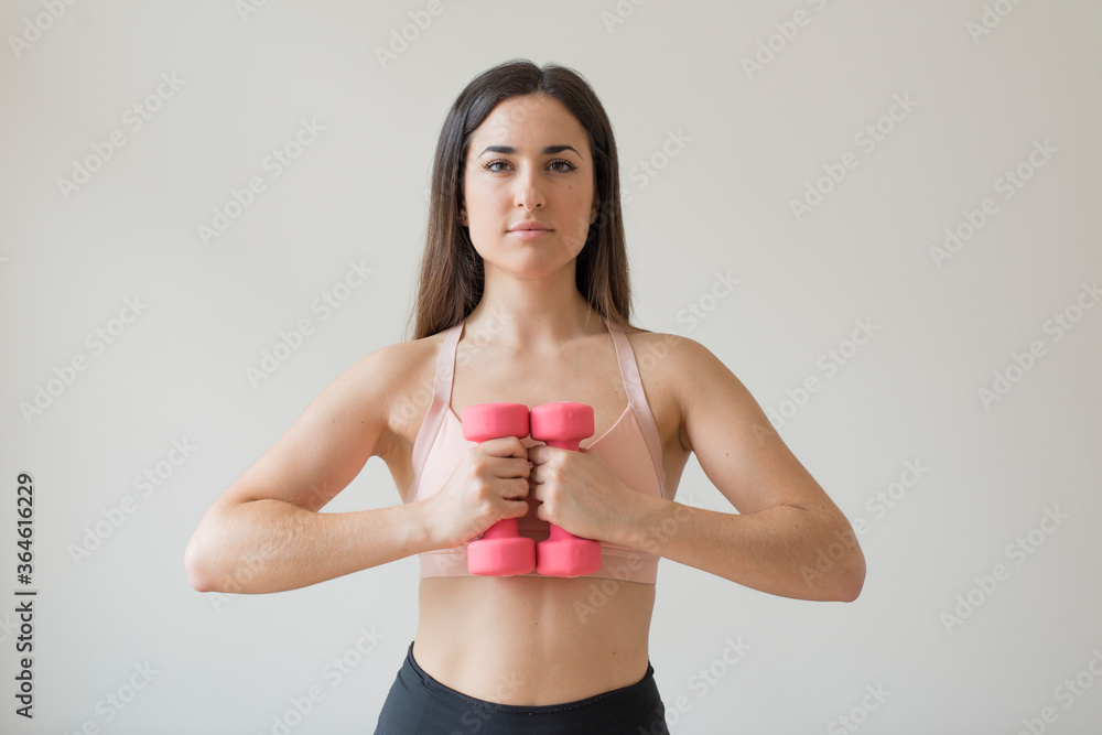 Fototapeta premium Young brunette woman exercising with pink dumbbells in front of a white background