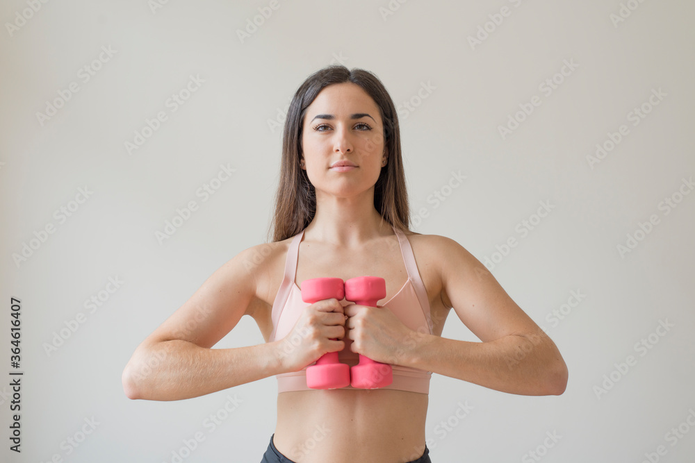 Young brunette woman exercising with pink dumbbells in front of a white background Young brunette woman exercising with pink dumbbells in front of a white background
