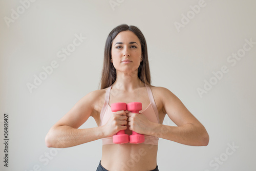 Young brunette woman exercising with pink dumbbells in front of a white background
