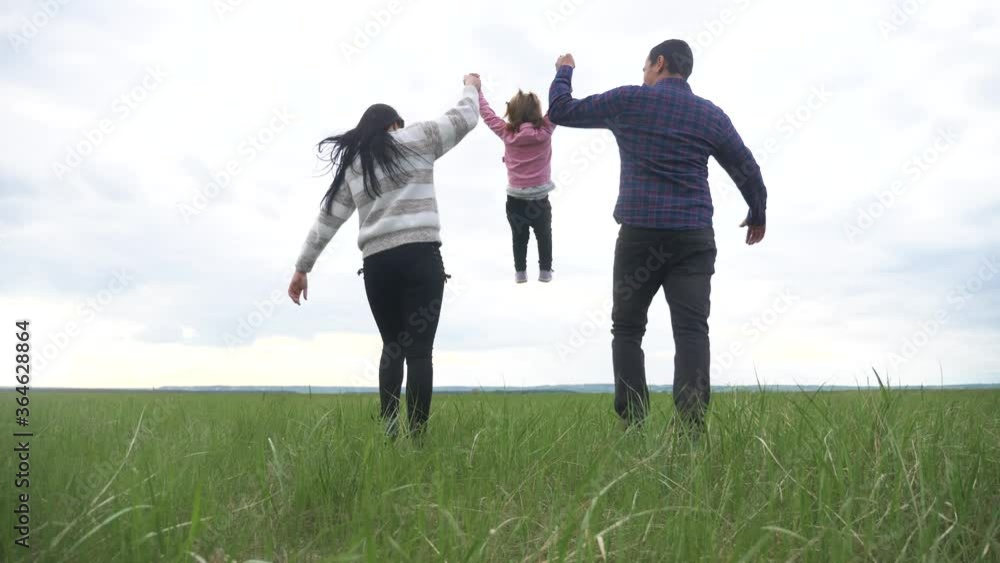 happy family. mom dad and little child a are running in the park raise hands play teamwork outdoors holding hands. woman man and little girl raise up hands on green field at lifestyle sunset happy family. mom dad and little child a are running in the park raise hands play teamwork outdoors holding hands. woman man and little girl raise up hands on green field at lifestyle sunset