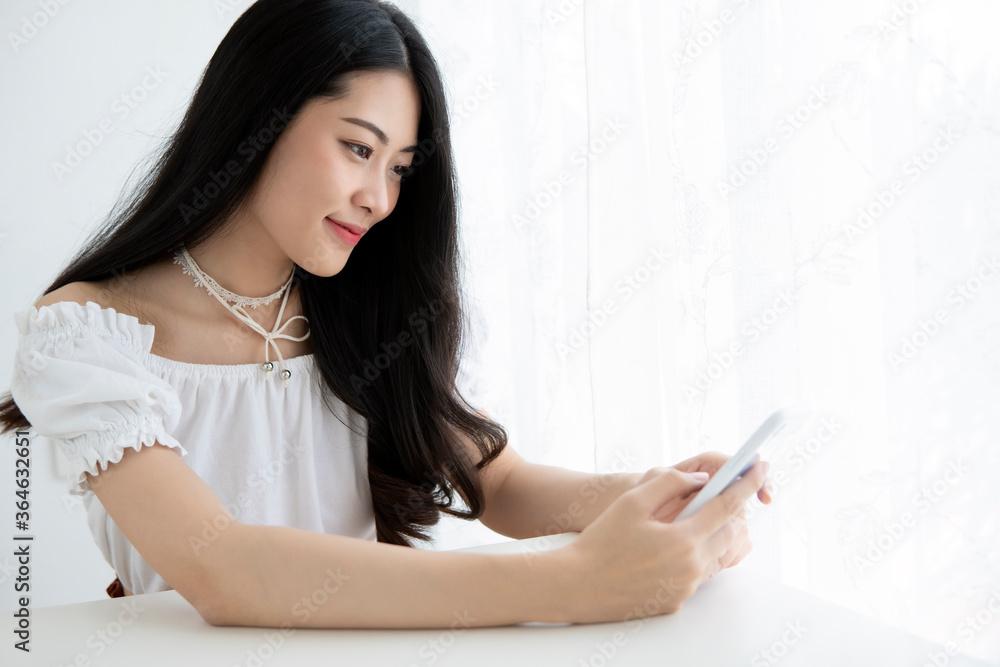 Asian woman is e-commerce entrepreneur sitting smiling and looking on smartphone in her house . Young woman's use a technology for life style . Asian woman is e-commerce entrepreneur sitting smiling and looking on smartphone in her house . Young woman's use a technology for life style .