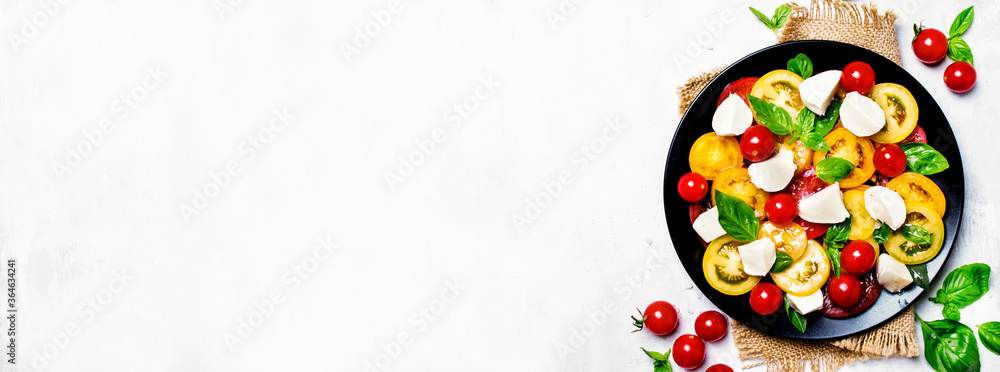 Salad of multi-colored tomatoes, mozzarella, and green basil, gray background, top view. Panoramic banner with copy space