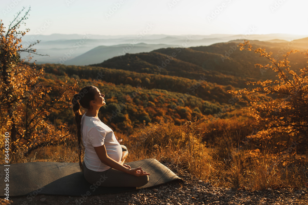 Pregnant woman in lotus position do yoga alone outdoors. Amazing autumn mountain view at sunset. Spiritual maternity concept, natural harmony.