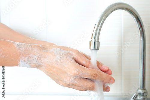 Hands of woman wash their hands in a sink with foam to wash the skin and water flows through the hands. Concept of health, cleaning and preventing germs and coronavirus from contacting hands