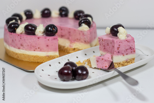 A piece of Cherry cheesecake on white plate with berries and tea spoon.