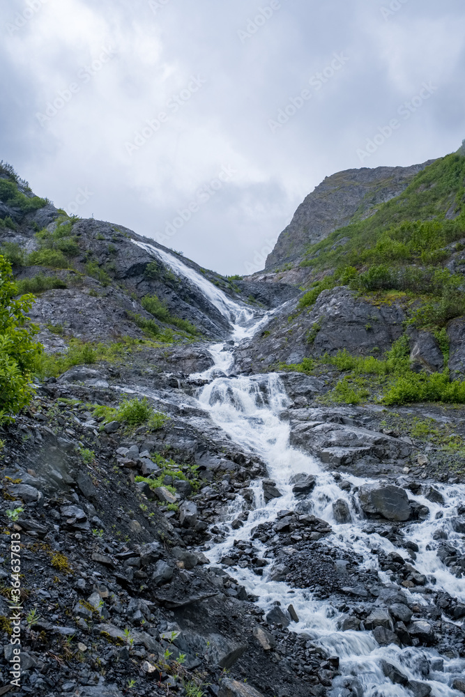 At the foot of an alpine waterfall, with the mountain towering above At the foot of an alpine waterfall, with the mountain towering above