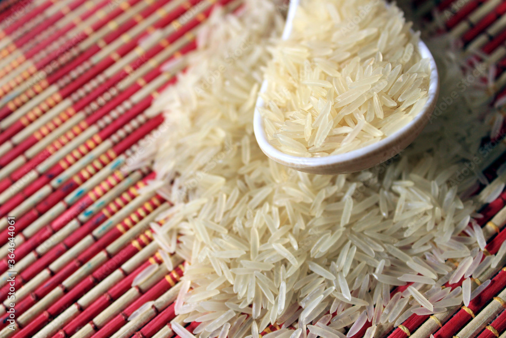 Rice grains in a white plastic spoon on multi color texture background. Macro background of white rice. Basmati rice on a pile isolated on colorful pattern background.