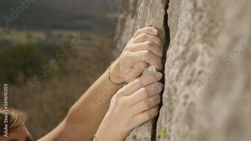 SLOW MOTION, CLOSE UP, DOF: Fit female lead climber holds on to a flake grip on a massive cliff. Athletic woman grips a crack with chalked up hands while bouldering in the mountains of Slovenia. photo