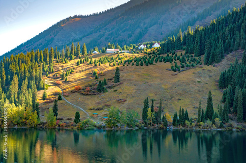 Kolsay (Kolsai) National Park, Lower Lake, Kazakhstan adventure travel, Scenic landscape, view over lake in mountainous wood with huge Tian Shan pine trees, village on the op of the hill