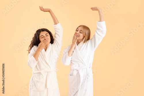 Beautiful young women in bathrobes on color background