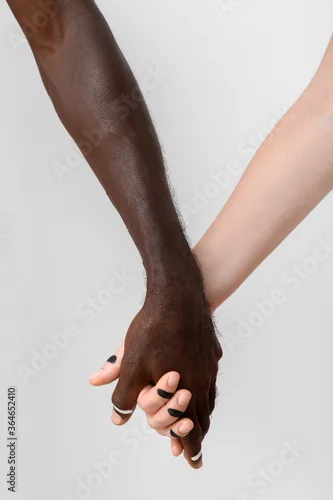 Obraz Caucasian woman and African-American man holding hands together on light background. Racism concept