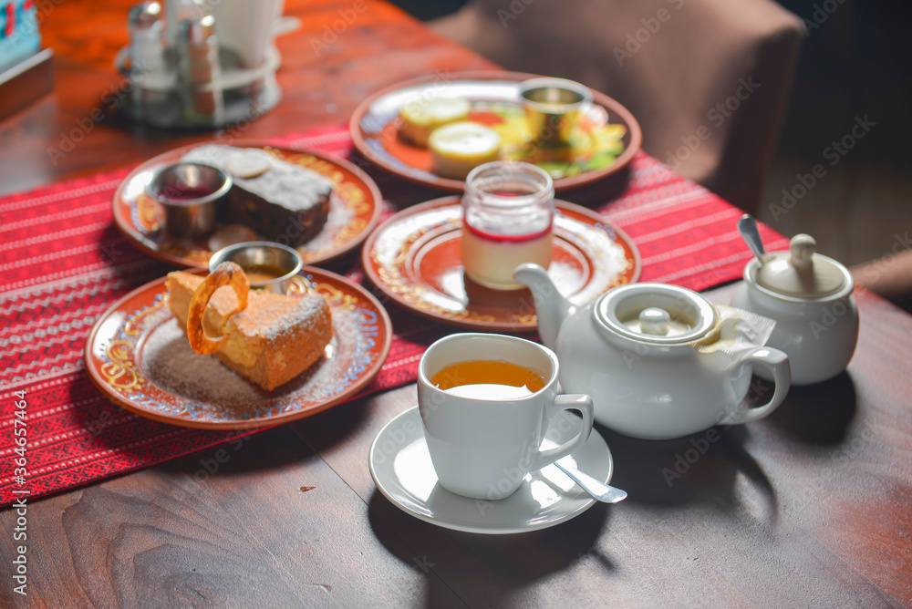 Table set for tea time with sweet desserts. Chocolate brownie cake, vanilla cake, panna cotta. Tea pot with sweet tea. Table set for tea time with sweet desserts. Chocolate brownie cake, vanilla cake, panna cotta. Tea pot with sweet tea.