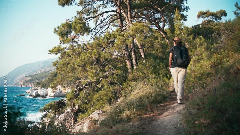 Cinematic 4k shot. A young woman backpacker walking in the forest with a sea view along the hiking trail and enjoying the view. Cinematic 4k shot. A young woman backpacker walking in the forest with a sea view along the hiking trail and enjoying the view.