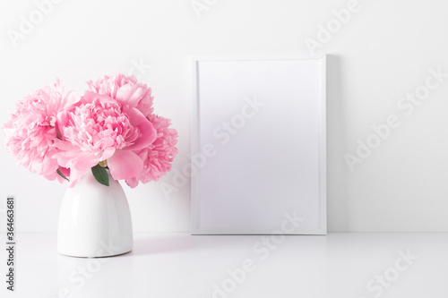 Fototapeta Naklejka Na Ścianę i Meble -  Home interior floral decor with pink peonies on white shelf. Front view blank mock up of photo frame. Beautiful flowers pink peonies in vase on white background