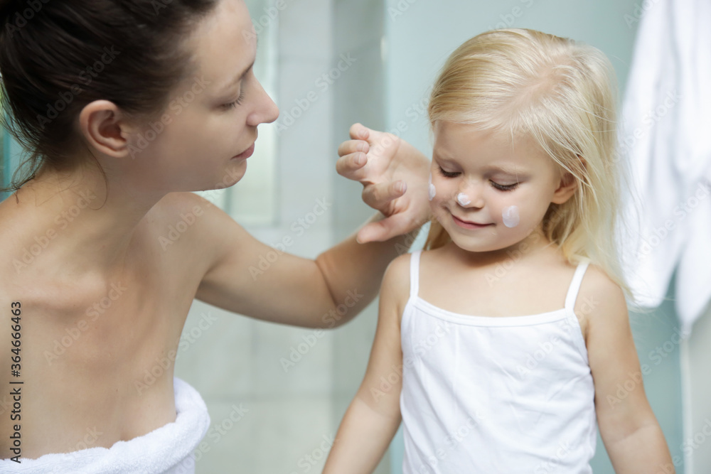Mom applying cream on her daughter face in bathroom. 