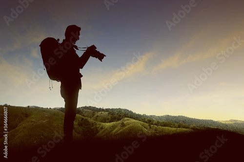 Silhouette of a man with a backpack holding the camera on the top of the hills