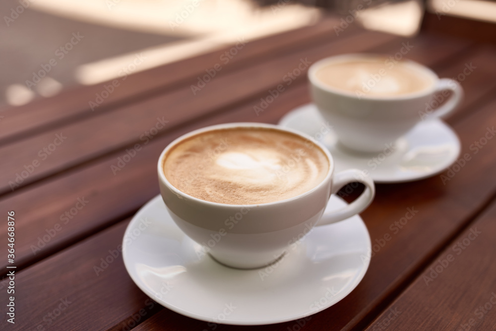 Two cups of cappuccino on the wooden background. Beautiful brown foam, white ceramic cups, place for text Two cups of cappuccino on the wooden background. Beautiful brown foam, white ceramic cups, place for text