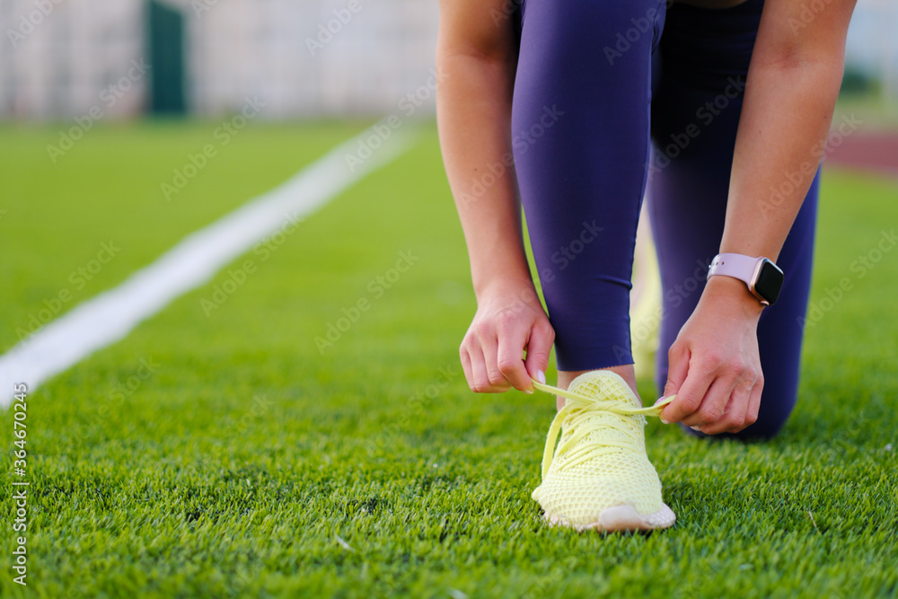 A young beautiful dark-cheeked woman in sportswear is engaged in fitness at the city stadium outdoors. A green football field.
