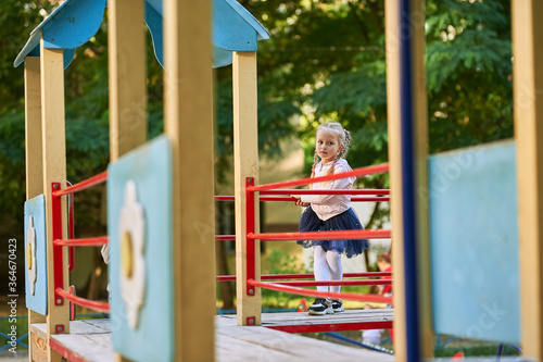 a little girl with blond hair plays on the playground and climbs on the game slides and steps of the house