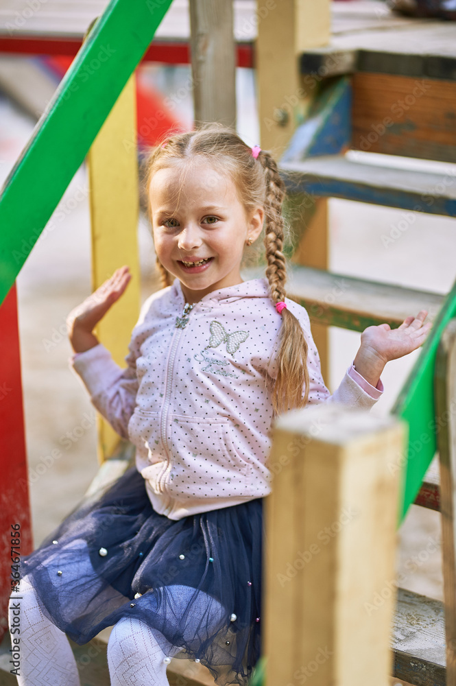 Little girl alone sits on the playground on the steps of the playhouse and laughs Little girl alone sits on the playground on the steps of the playhouse and laughs