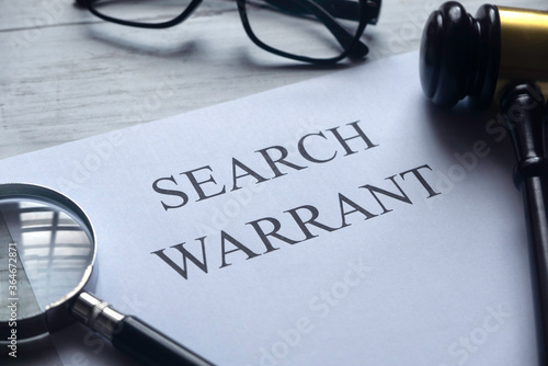 Selective focus of magnifying glass,gavel,glasses and paper written with Search Warrant on white wooden background. photo