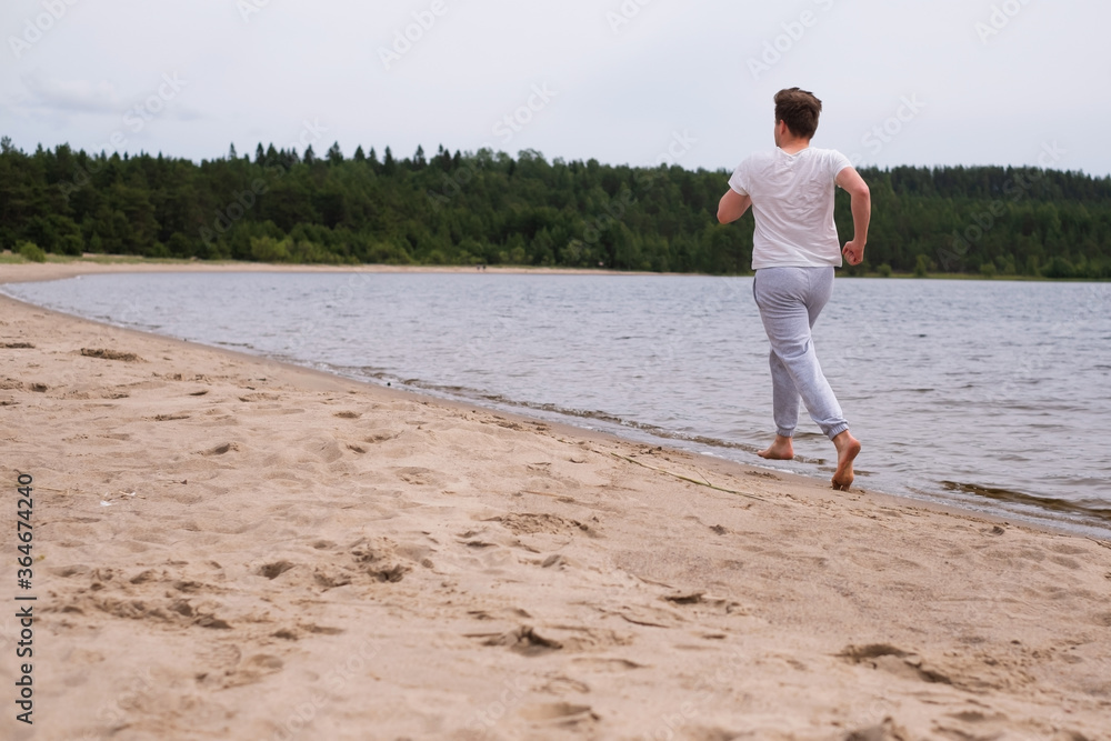 Young caucasian man in fitness clothing running along sandy beach. Rear view