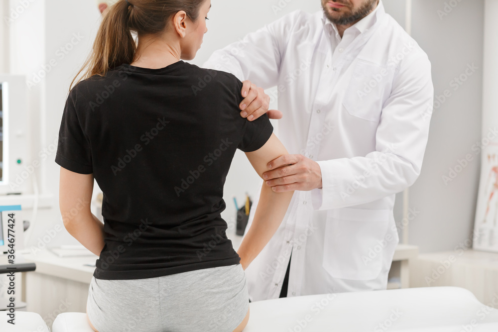 Fototapeta premium Male doctor examining female patient suffering from elbow pain. Medical exam. Chiropractic, osteopathy, post traumatic rehabilitation,sport physical therapy. Alternative medicine, pain relief concept.