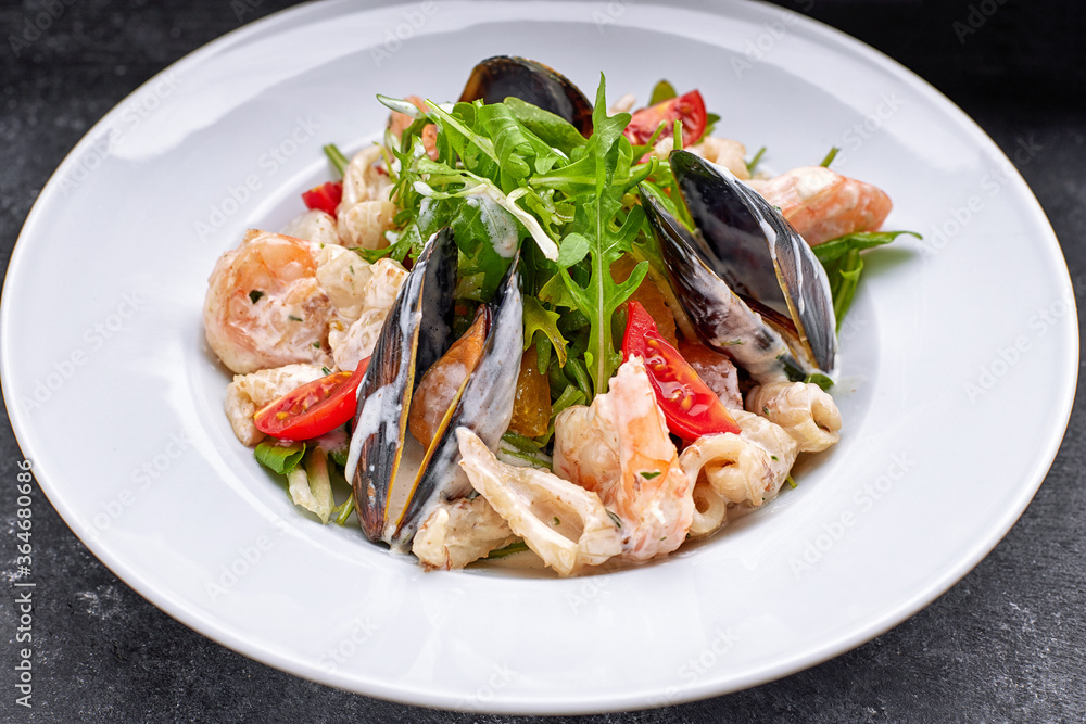 Seafood salad with mussels, squid, shrimp, on a round white plate, on a gray background