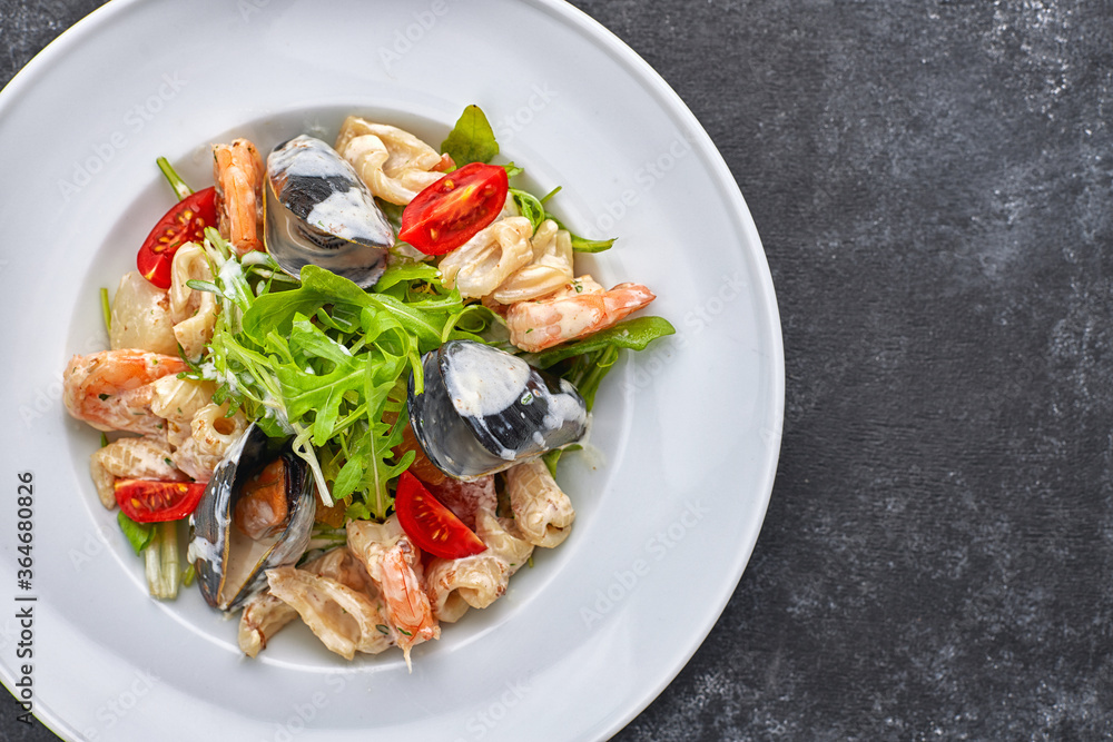 Seafood salad with mussels, squid, shrimp, on a round white plate, on a gray background Seafood salad with mussels, squid, shrimp, on a round white plate, on a gray background