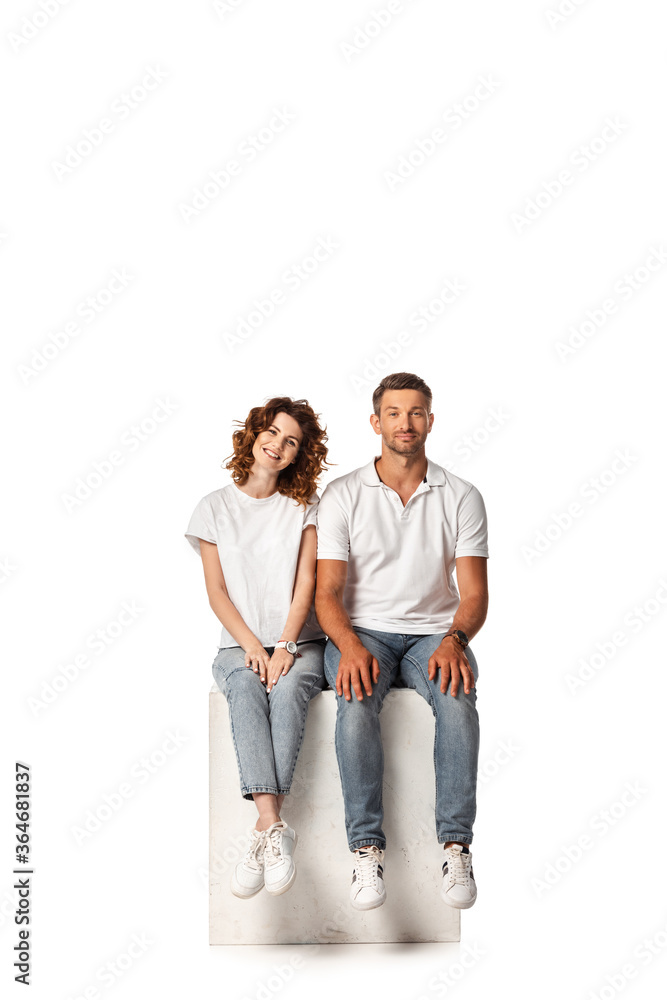 cheerful couple smiling and sitting on cube on white cheerful couple smiling and sitting on cube on white