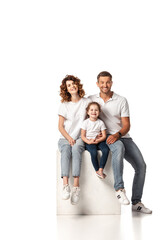 cheerful family smiling and sitting on cube on white