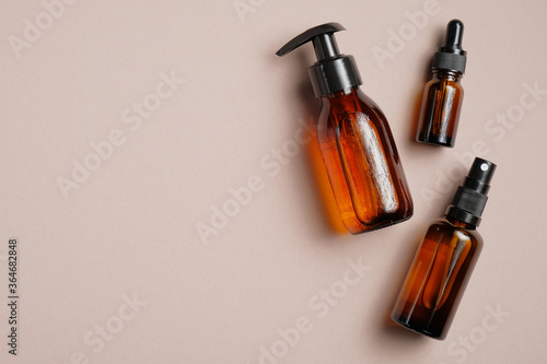 Set of amber glass cosmetic bottles on brown background. Pump bottle, dropper bottle, dispenser cosmetic container Flat lay, top view.