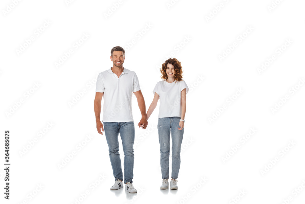 happy woman and cheerful man holding hands and standing on white