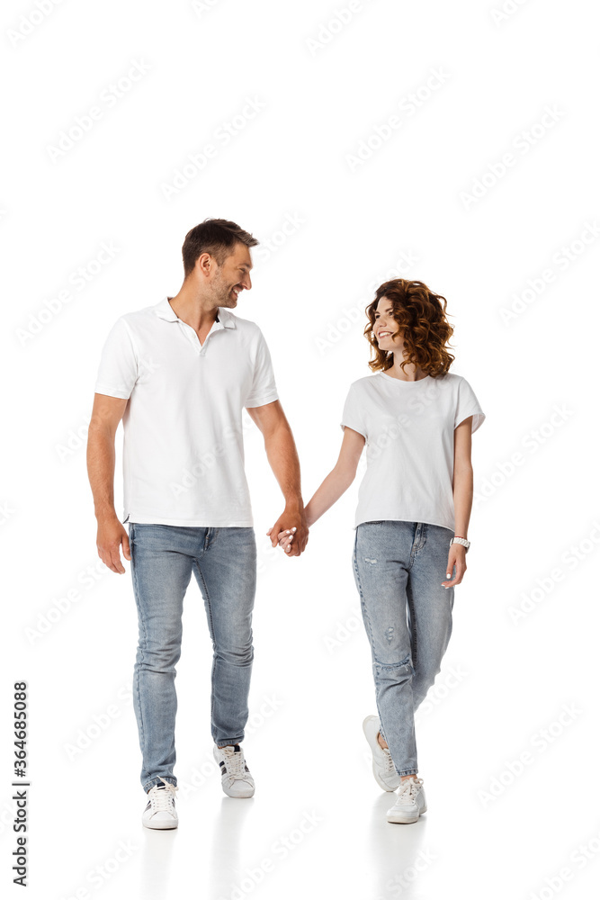 happy woman and cheerful man holding hands and looking at each other while walking on white happy woman and cheerful man holding hands and looking at each other while walking on white