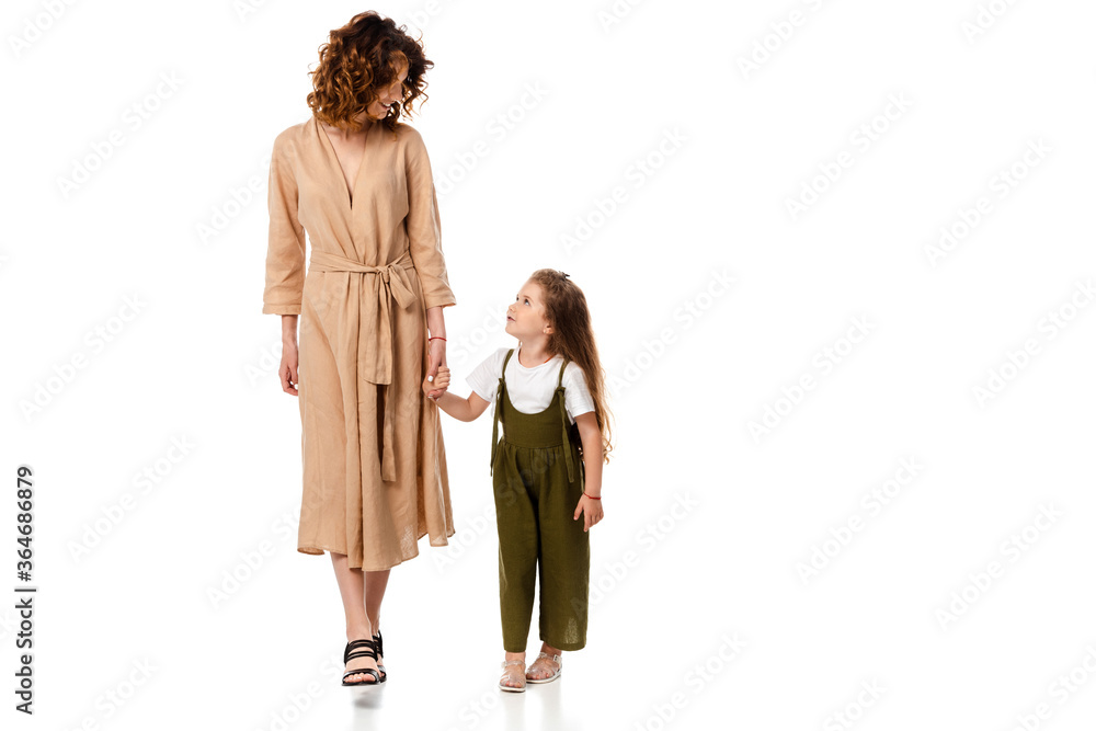 cheerful mother and adorable daughter holding hands isolated on white