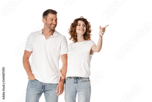 happy man standing with hand in pocket near curly woman pointing with finger isolated on white
