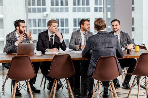 young confident caucasian men gathered to hold business meeting together, to discuss new business ideas and strategies , to share experiences and opinions , isolated in modern office