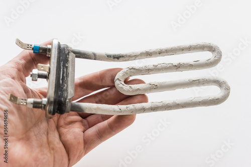 Damaged heating element of the washing machine in a hand on a white background.