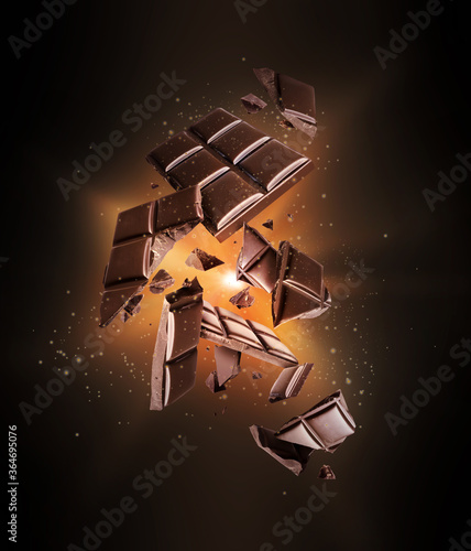 Bar of dark chocolate crushed in the air with flash of light in the dark