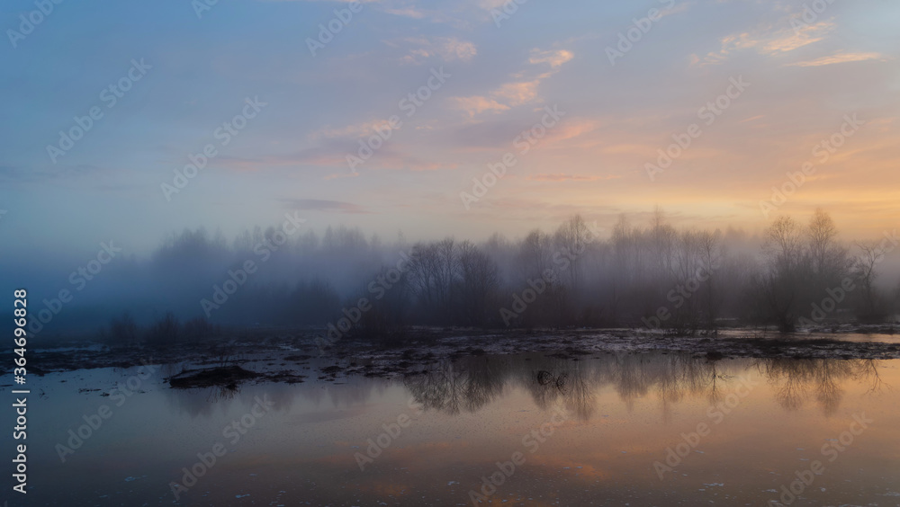 Sunset and forest lake, colorful dawn in the countryside, landscape with reflection in the water and rising fog.