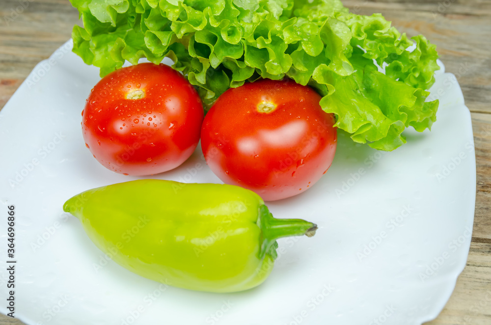 Fresh juicy vegetables peppers, tomatoes, cucumbers lettuce leaves with water drops beautifully laid out on a white plate close-up. Vegetables are in the form of a funny face Fresh juicy vegetables peppers, tomatoes, cucumbers lettuce leaves with water drops beautifully laid out on a white plate close-up. Vegetables are in the form of a funny face
