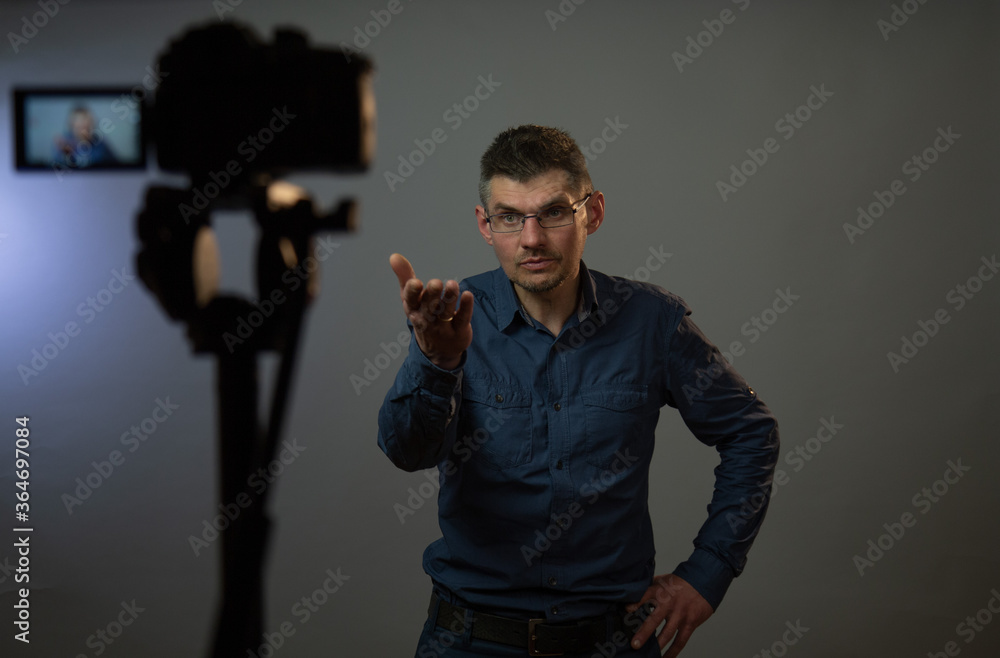 actor wearing glasses in grey shirt with interrogative look stretches hand ahead posing for blurry camera in studio closeup actor wearing glasses in grey shirt with interrogative look stretches hand ahead posing for blurry camera in studio closeup