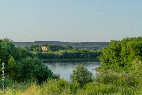 house stands on the Bank of a beautiful river among trees and bushes on a Sunny summer day. Beautiful scenery
